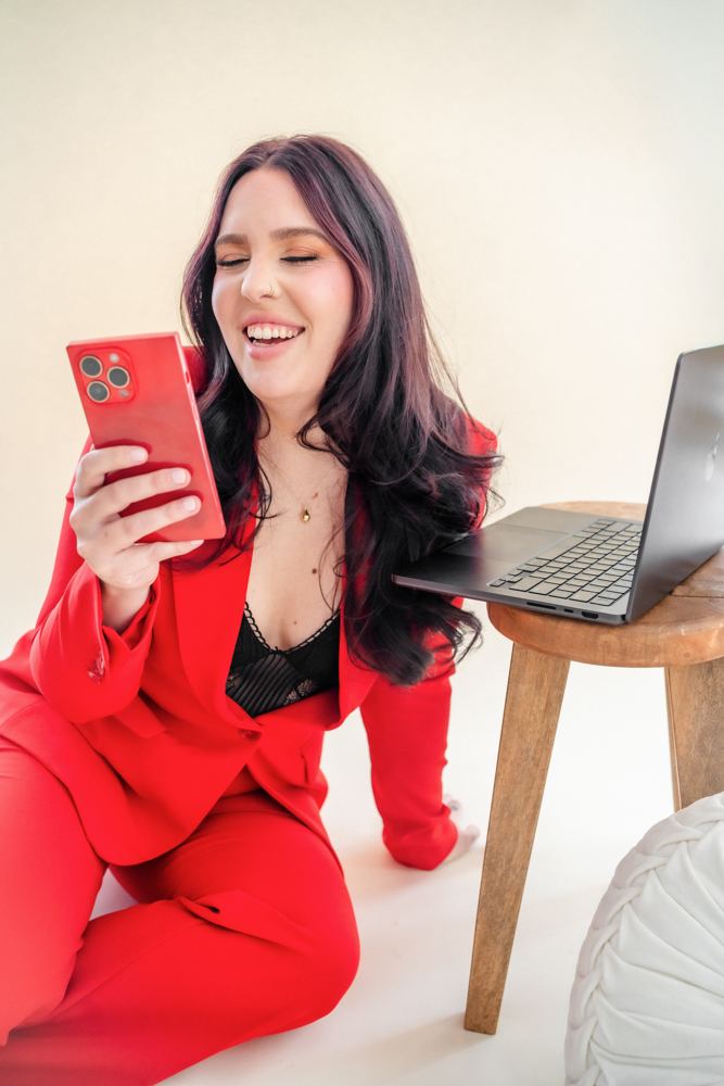 Sydney laughing at her phone in a red suit